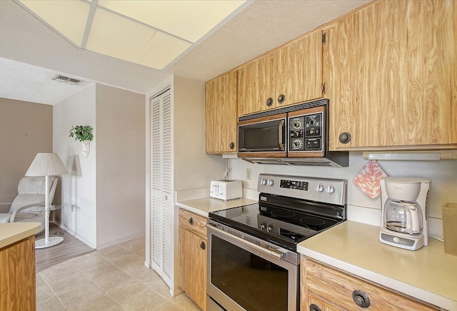 kitchen featuring visible vents, electric stove, light tile patterned flooring, black microwave, and light countertops