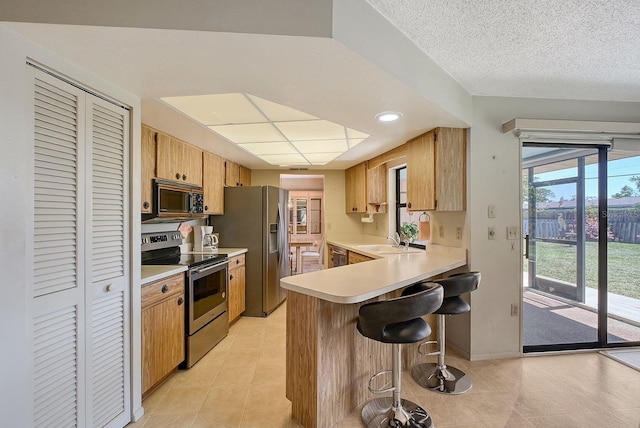 kitchen featuring a peninsula, a sink, light countertops, appliances with stainless steel finishes, and a kitchen bar