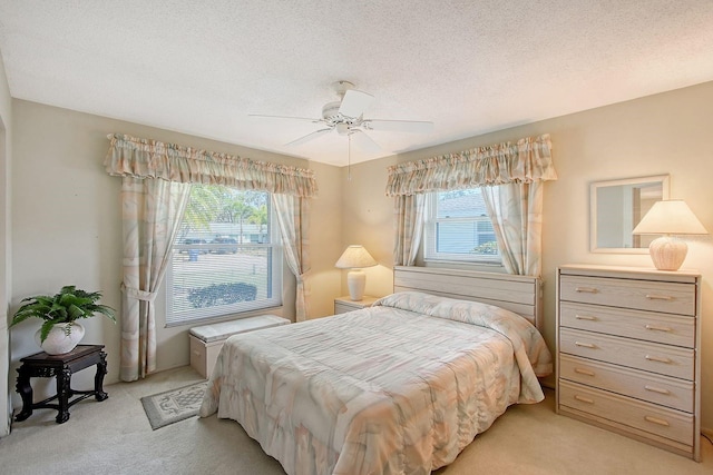 bedroom featuring light carpet, multiple windows, a textured ceiling, and a ceiling fan