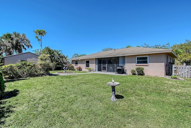 rear view of property with a yard, fence, a sunroom, and stucco siding