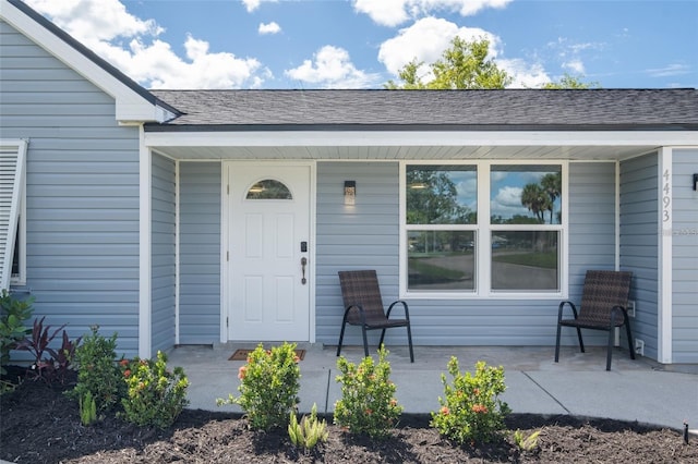 view of exterior entry featuring a patio and a shingled roof