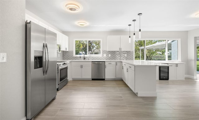 kitchen featuring beverage cooler, backsplash, stainless steel appliances, a peninsula, and light countertops