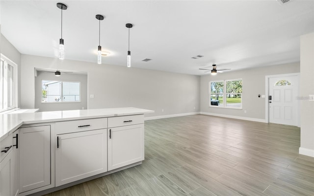 kitchen with light wood-type flooring, a ceiling fan, open floor plan, light countertops, and hanging light fixtures