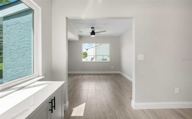 spare room with light wood-style flooring, a ceiling fan, and baseboards