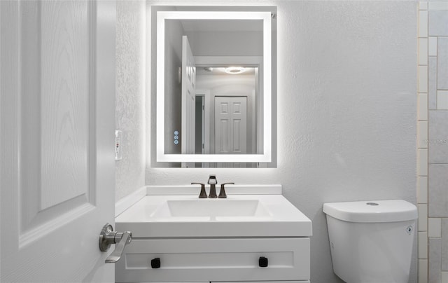 bathroom featuring vanity, toilet, and a textured wall