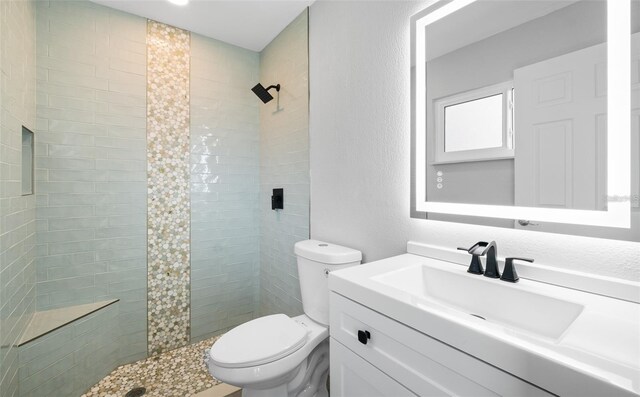 full bathroom with vanity, toilet, a textured wall, and tiled shower