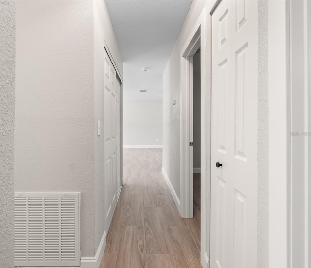 hall featuring light wood-style flooring, baseboards, visible vents, and a textured wall