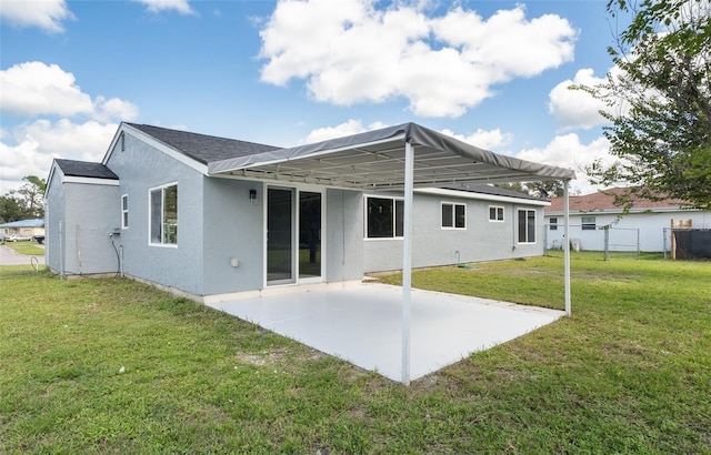 rear view of property with stucco siding, fence, a lawn, and a patio area