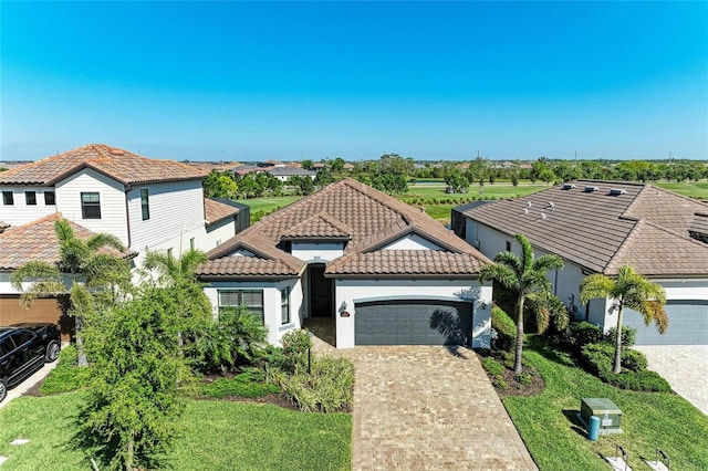 mediterranean / spanish-style home with decorative driveway, a tile roof, an attached garage, and stucco siding