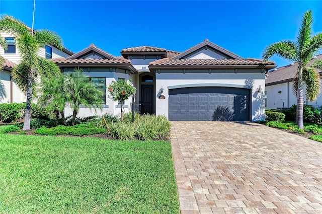 mediterranean / spanish-style house with stucco siding, a front lawn, a garage, a tiled roof, and decorative driveway