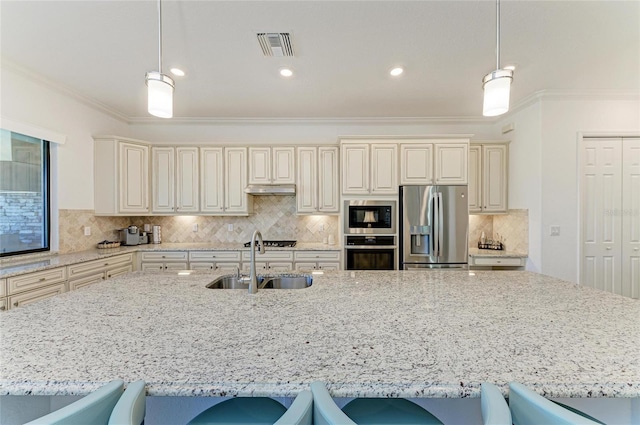 kitchen featuring a sink, appliances with stainless steel finishes, cream cabinets, crown molding, and a kitchen breakfast bar