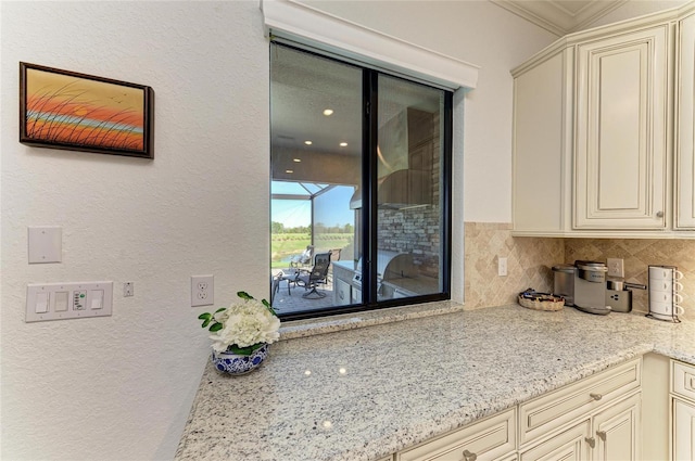 kitchen with light stone counters, backsplash, cream cabinetry, and a textured wall