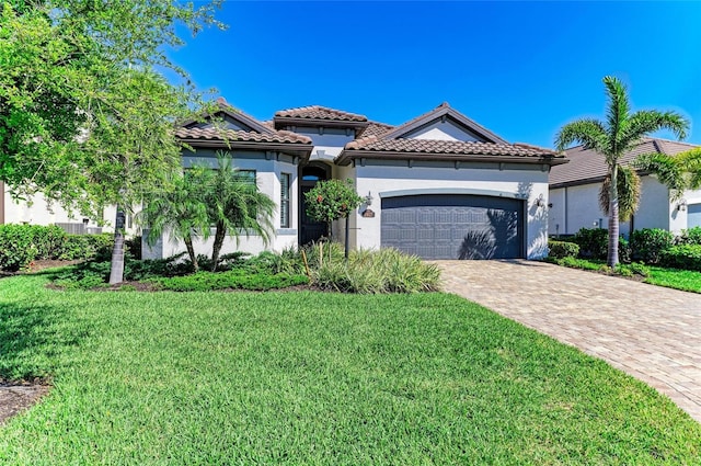 mediterranean / spanish home with a tile roof, a front yard, stucco siding, decorative driveway, and a garage