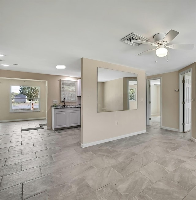 unfurnished living room with a ceiling fan, a sink, baseboards, and visible vents