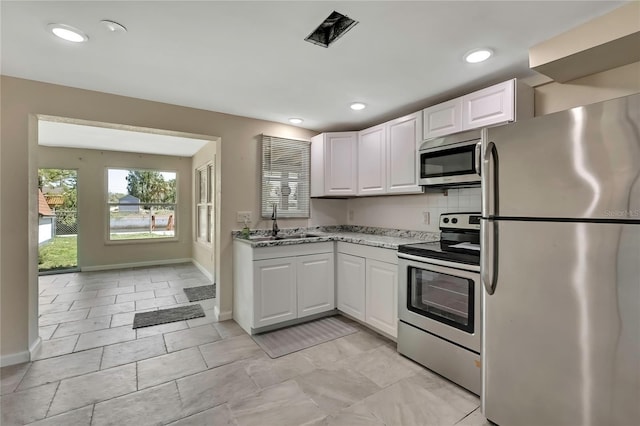 kitchen featuring tasteful backsplash, a sink, white cabinets, light stone countertops, and appliances with stainless steel finishes