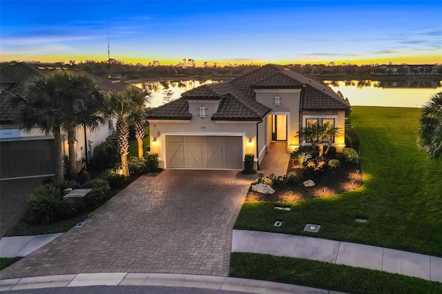 mediterranean / spanish-style house with a tiled roof, a front yard, stucco siding, decorative driveway, and an attached garage