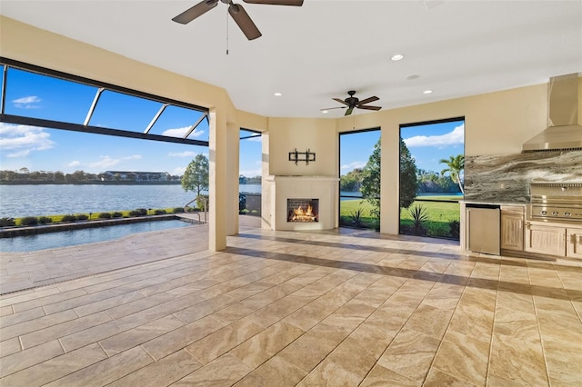 view of patio / terrace featuring a water view, a ceiling fan, a tiled fireplace, exterior kitchen, and a lanai