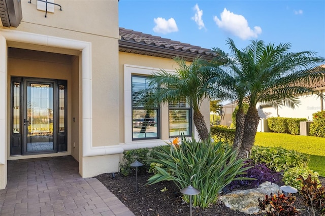 view of exterior entry with a tile roof and stucco siding