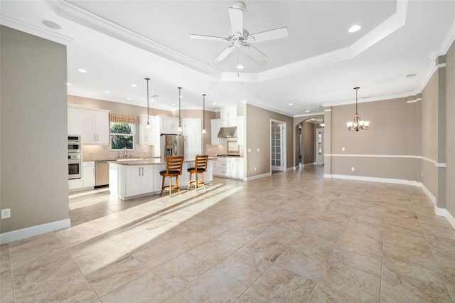 unfurnished living room featuring baseboards, a sink, crown molding, a raised ceiling, and ceiling fan with notable chandelier