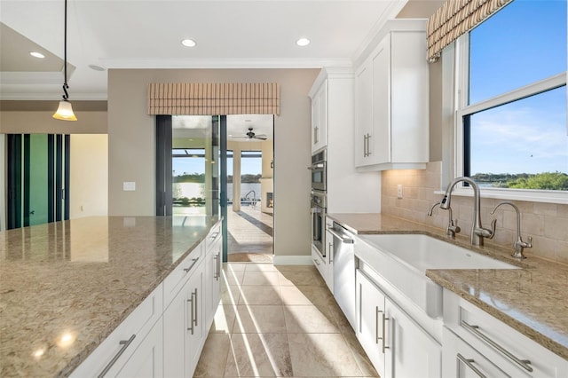 kitchen with backsplash, crown molding, light stone countertops, white cabinets, and a sink