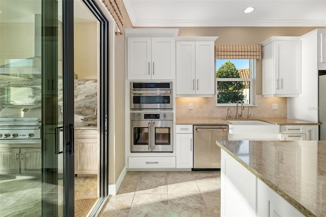 kitchen with light stone countertops, appliances with stainless steel finishes, white cabinetry, and ornamental molding