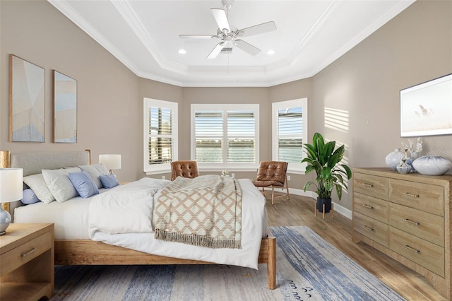 bedroom with a raised ceiling, wood finished floors, baseboards, and ornamental molding