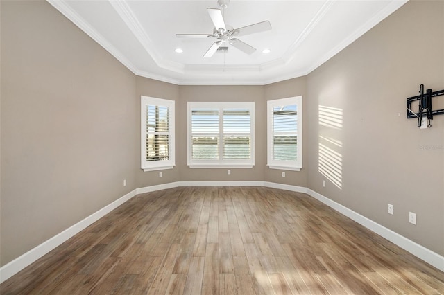 empty room featuring ornamental molding, a raised ceiling, baseboards, and wood finished floors