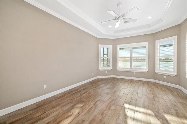 spare room featuring crown molding, baseboards, light wood-type flooring, a tray ceiling, and a ceiling fan