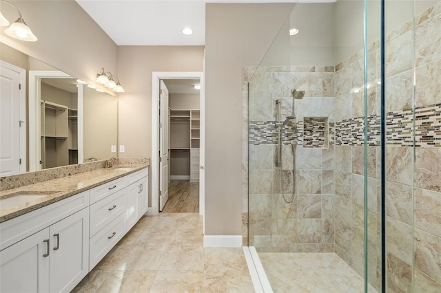 bathroom with a walk in closet, double vanity, a tile shower, and a sink