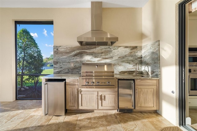 kitchen featuring light stone counters, light brown cabinets, a sink, extractor fan, and appliances with stainless steel finishes