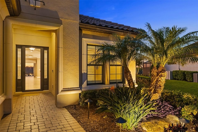 view of exterior entry featuring stucco siding and a tile roof