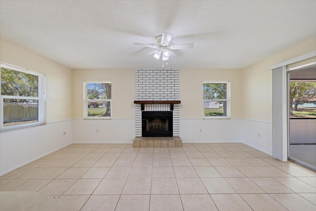 unfurnished living room with a textured ceiling, ceiling fan, a wainscoted wall, and a tile fireplace