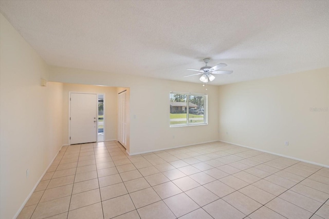 empty room featuring light tile patterned floors, baseboards, a textured ceiling, and a ceiling fan