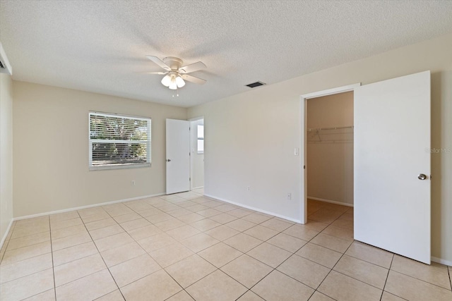 unfurnished bedroom featuring a ceiling fan, visible vents, light tile patterned flooring, a closet, and a walk in closet