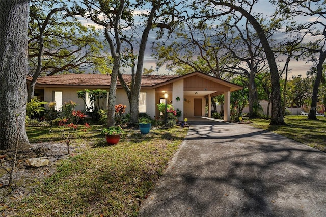 view of front facade featuring a carport, a lawn, driveway, and stucco siding