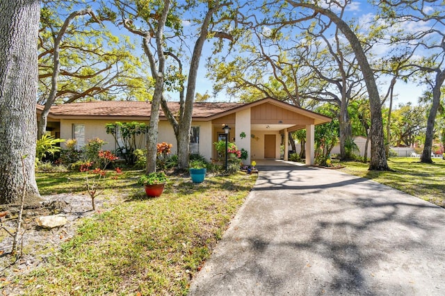 view of front facade featuring stucco siding, a carport, concrete driveway, and a front yard