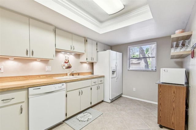 kitchen featuring a tray ceiling, ornamental molding, light tile patterned floors, white appliances, and a sink