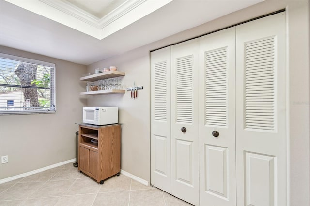 interior space with light tile patterned flooring, a raised ceiling, baseboards, and ornamental molding