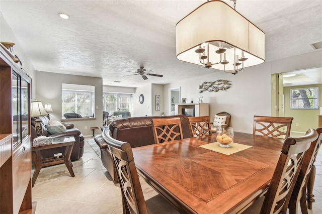 dining room featuring light tile patterned floors, a ceiling fan, baseboards, a fireplace, and a textured ceiling