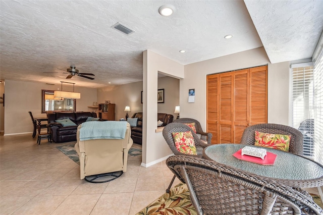 living area featuring light tile patterned floors, visible vents, baseboards, and a textured ceiling