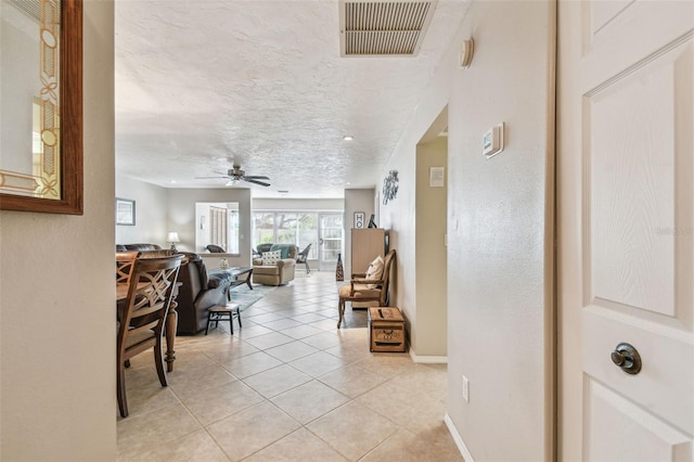 corridor with light tile patterned floors, visible vents, a textured ceiling, and baseboards