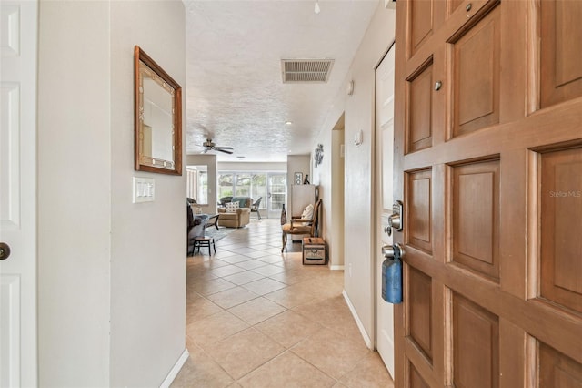 entryway featuring visible vents, a textured ceiling, light tile patterned floors, baseboards, and ceiling fan