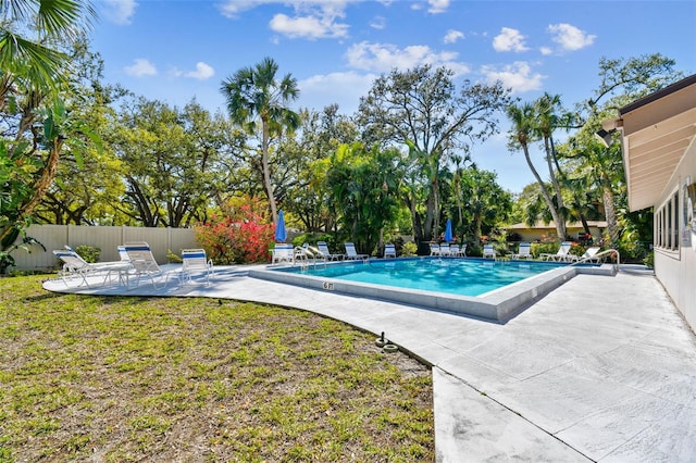 community pool with a patio area, a lawn, and fence