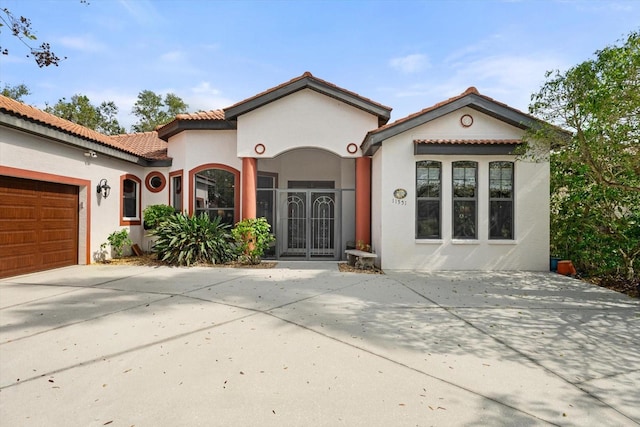 mediterranean / spanish-style home with stucco siding, a garage, concrete driveway, and a tiled roof