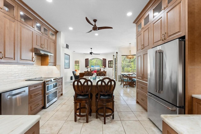 kitchen with light tile patterned floors, glass insert cabinets, under cabinet range hood, appliances with stainless steel finishes, and backsplash