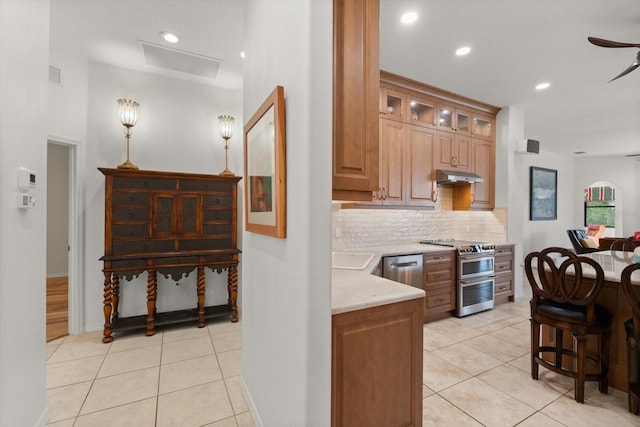 kitchen featuring visible vents, under cabinet range hood, light tile patterned floors, decorative backsplash, and stainless steel appliances