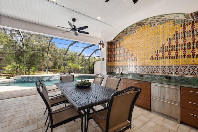 view of patio featuring glass enclosure, a ceiling fan, an outdoor kitchen, outdoor dining area, and an outdoor pool