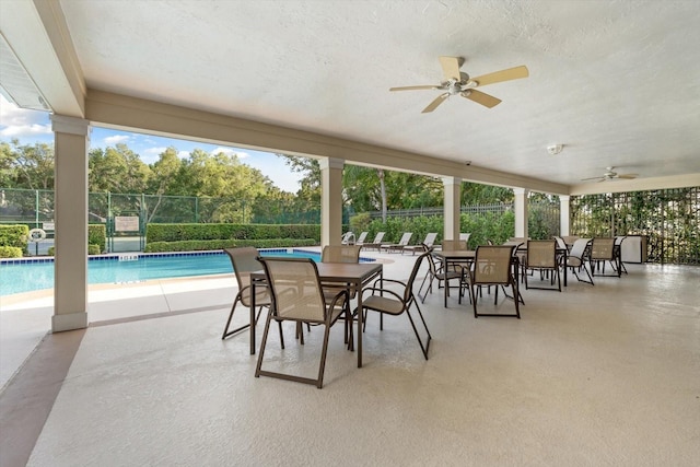 view of patio with a community pool, fence, and ceiling fan