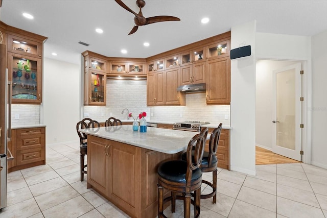 kitchen featuring under cabinet range hood, a kitchen bar, visible vents, and light tile patterned flooring