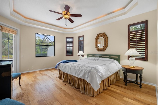 bedroom featuring light wood-style flooring, a raised ceiling, and multiple windows